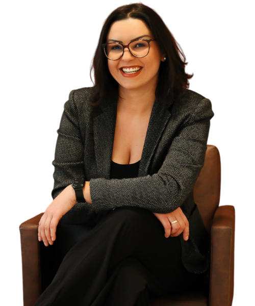 Natally Buzzatto, psicóloga, sentada em poltrona, sorrindo, usando óculos e blazer escuro.