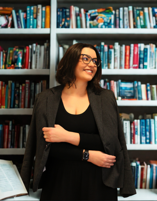 Natally Buzzatto, psicóloga, em frente a uma estante de livros.